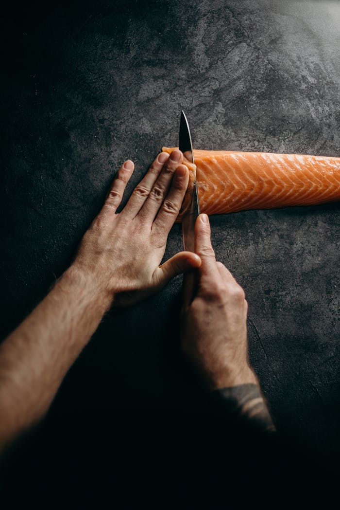 about-us-02 Chef expertly slicing fresh salmon on dark surface, highlighting culinary skill and precision in food preparation.